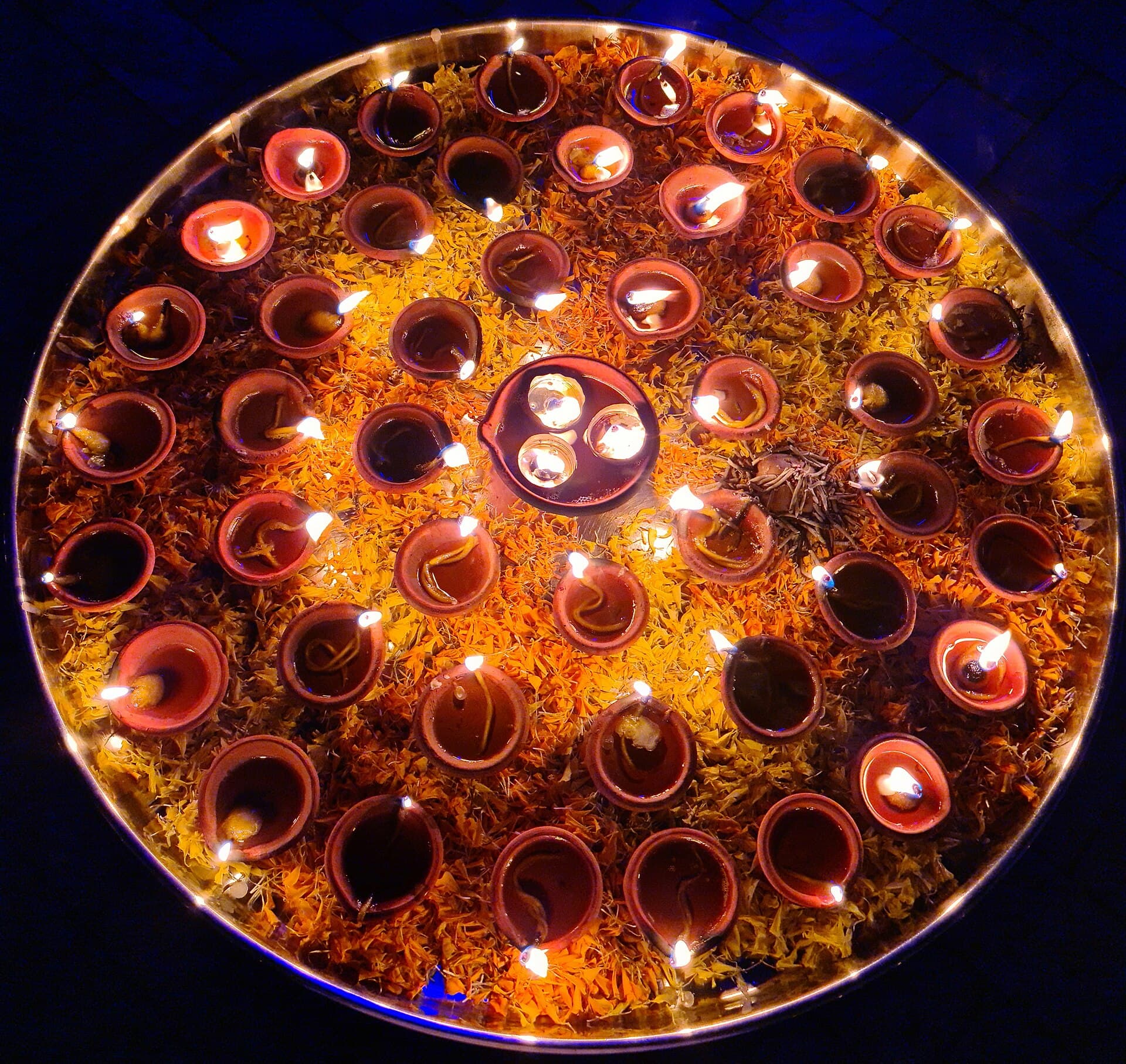 Pooja thali with flowers, sacred powders and a lit diya